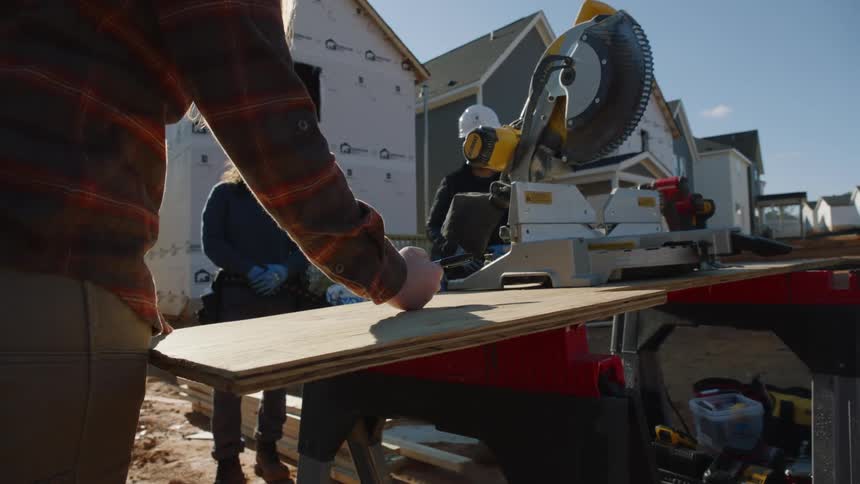 A group of construction workers stand on a site as one person draws on wood