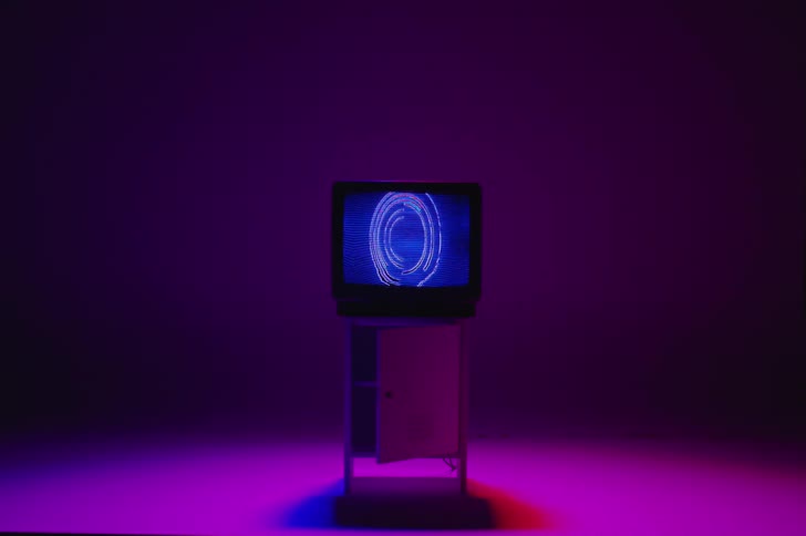 Circular objects rotate with flashing static on the blue screen of a television sitting on a floor illuminated with a magenta colored light