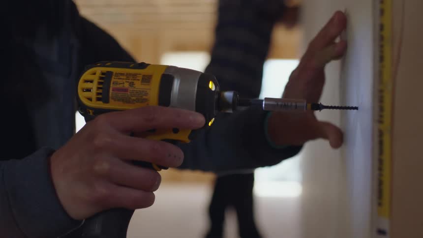 A construction worker drills a screw in to a wall