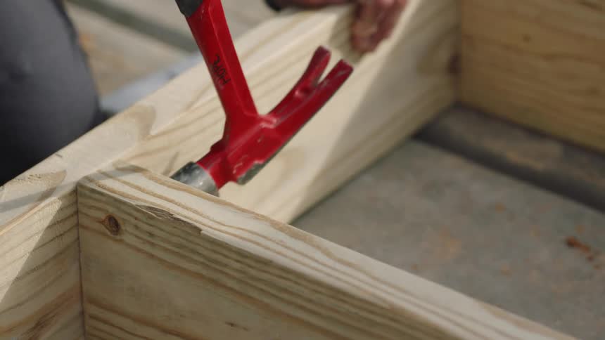 A construction worker is using a hammer to get a piece of wood into place on a frame