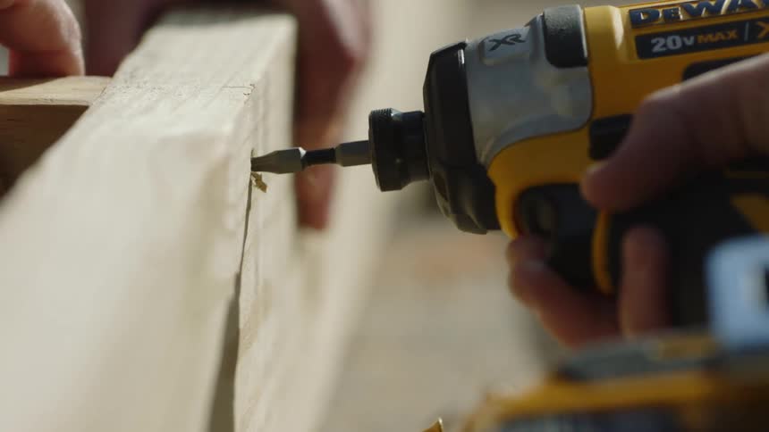 A man uses a drill to drill screws in to wood