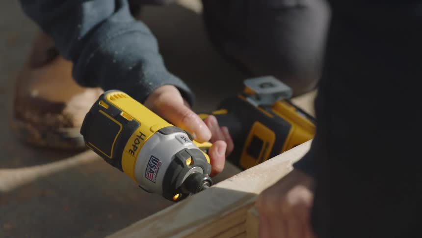 Worker uses power tool to drive screw into wooden frame lying on ground