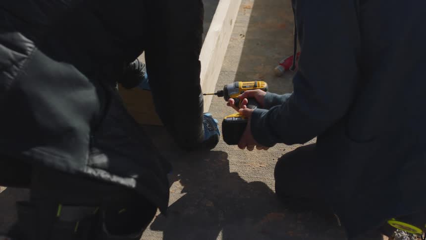 One person holds two pieces of wood as another drills them together