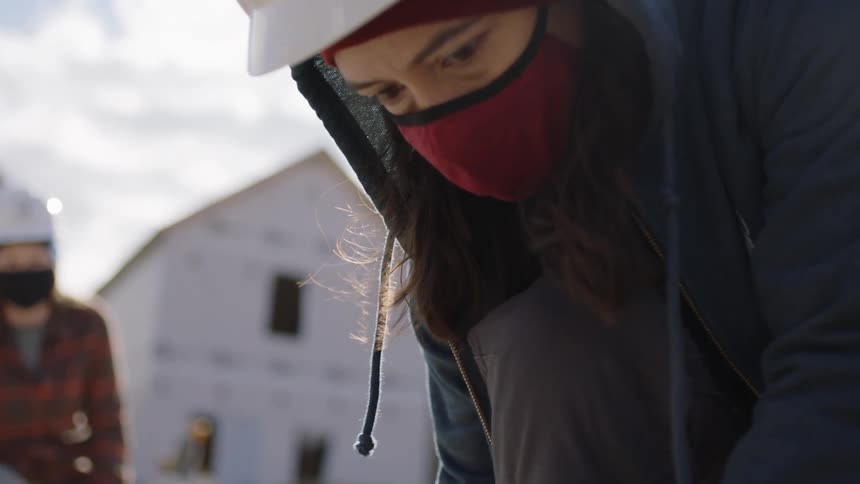 A woman marks wood with a pencil at a construction site
