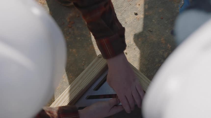 A pair of construction workers collaborate while assembling a wooden frame