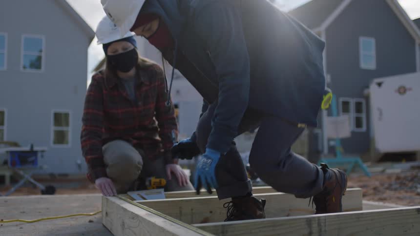 Construction workers hold and mark wooden frame lying on ground at construction site