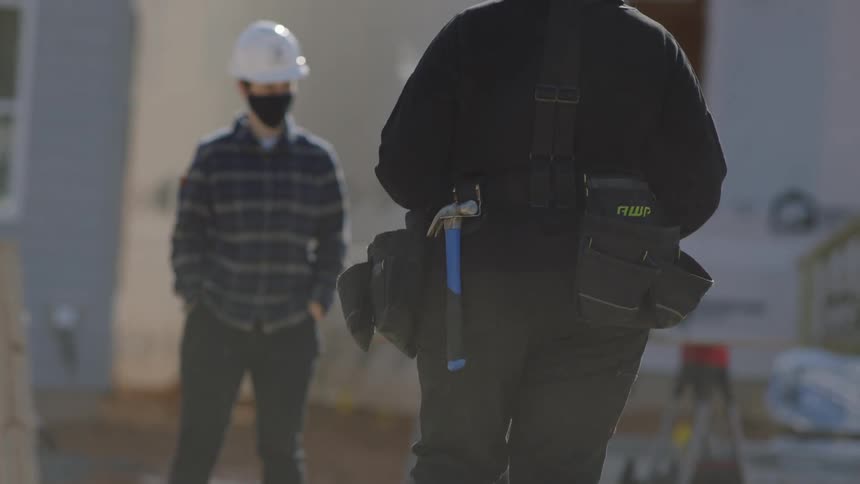 Construction workers are on site and a worker with their back turned has a hammer on their belt