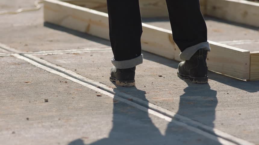 A person wearing work boots stands near some wooden beams that are affixed to each other