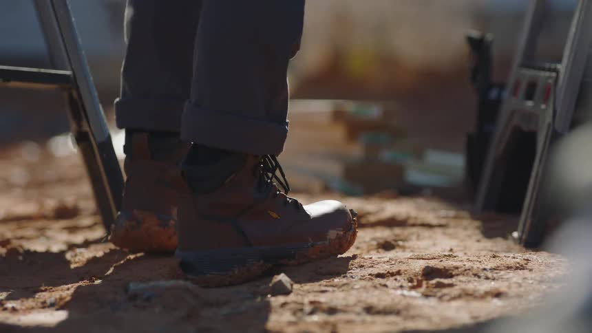 A person wearing sturdy work boots stands outdoors at a construction site