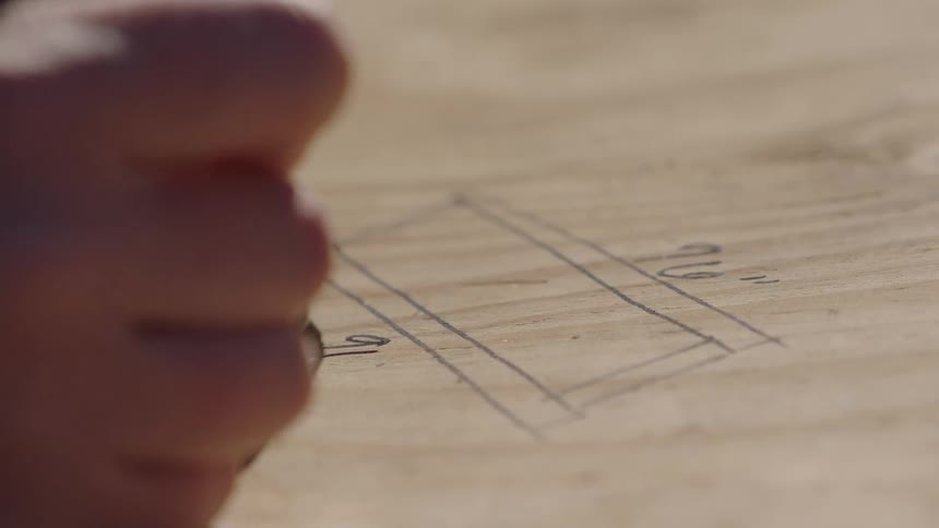 A construction worker is writing numbers and measurements on a piece of wood with a pen