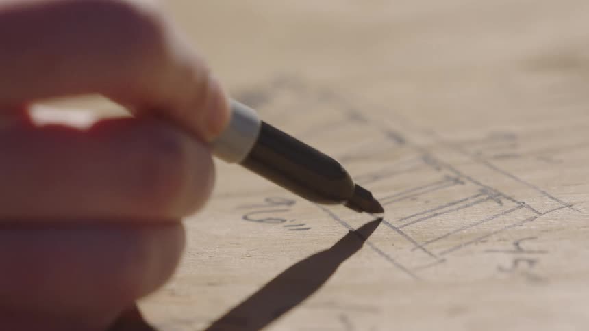 A man draws on a slab of wood with a marker