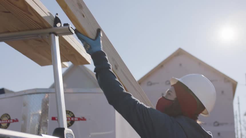 A man hands a piece of plywood down to a woman on a construction site