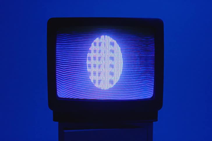 Designs in an oval shape with blue static lines move on a television screen sitting in a blue room