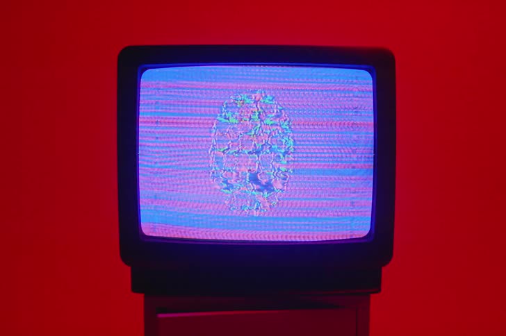 An oval shape in pink and blue static move on a television screen sitting in a red room