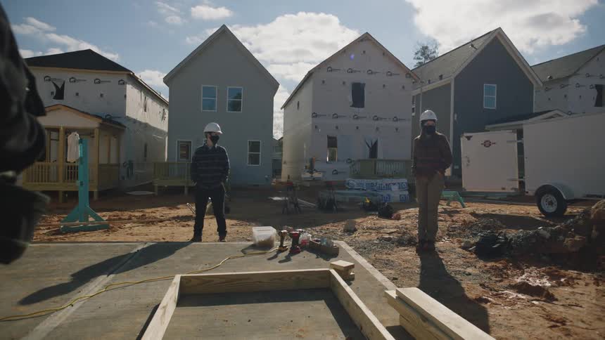 Two construction workers stand at home construction site near wooden frame