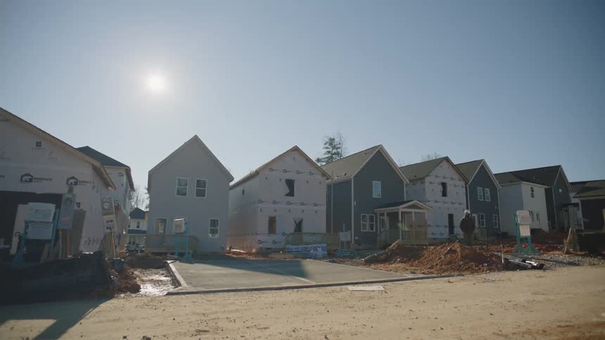 The sun shines brightly above houses being built in a new housing development as a construction worker stands outside