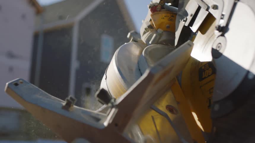A construction worker places a miter saw on a table outside a home