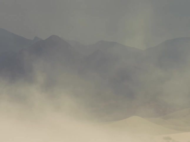 Silhouettes of mountains are seen through clouds as they move in the sky