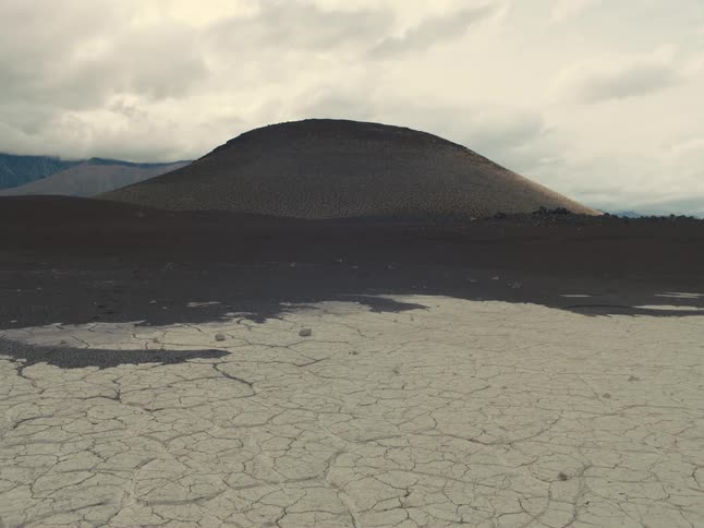 Cracks on the ground and a mountain in the distance under a cloudy sky
