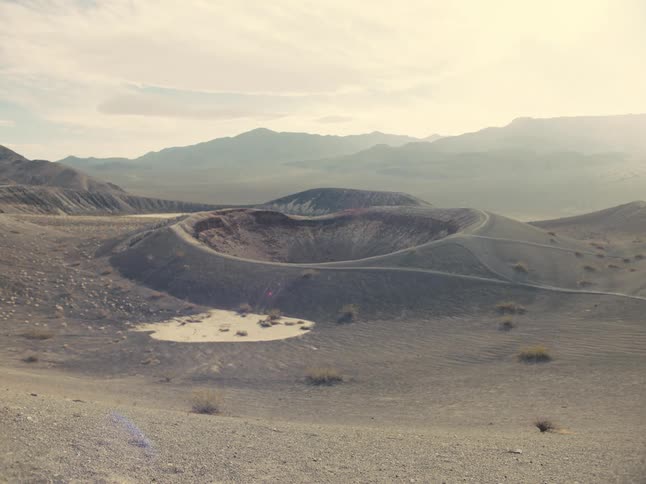 Crater sits near small pond in valley near fog covered mountains