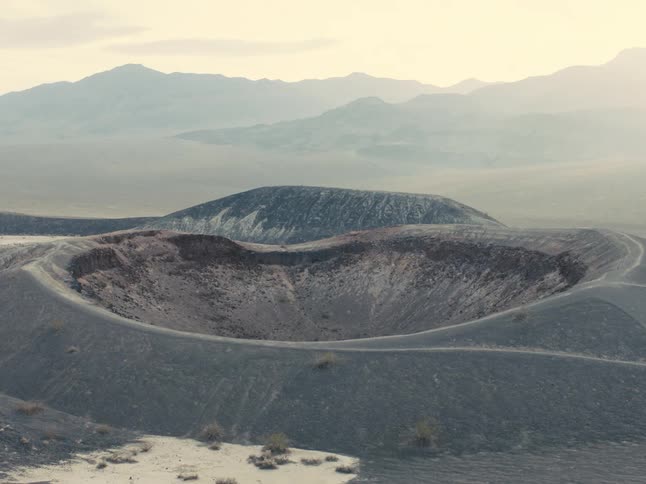 Crater stands near fog covered mountains under a red tinted sky