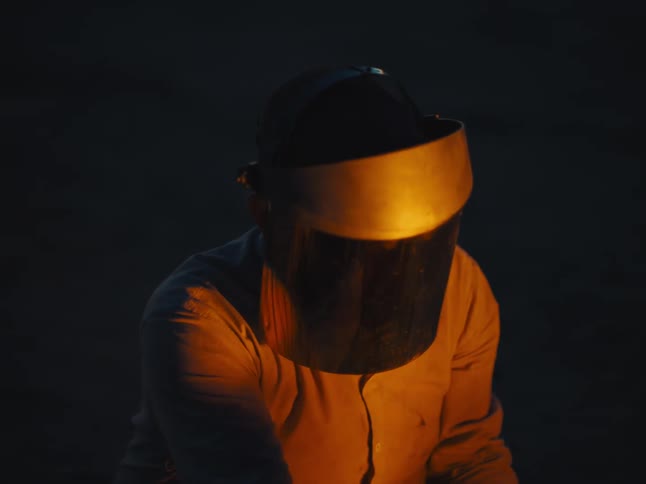The flare from a welder lights up a man with a shield over his face