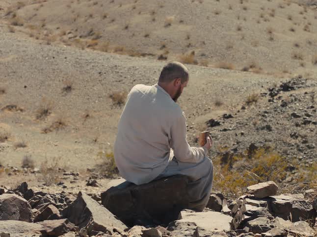 A man is sitting on a large rock holding a smaller rock
