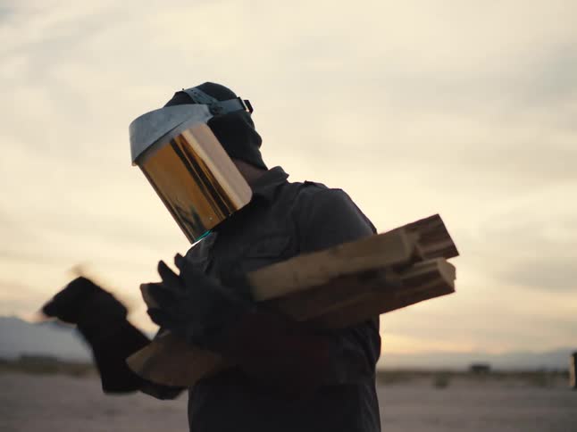A man with a shield over his face sets pieces of wood outside