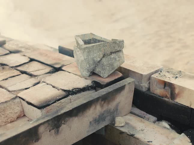 Smoke and dust rises from soot covered bricks as angular pot sits on brick surface