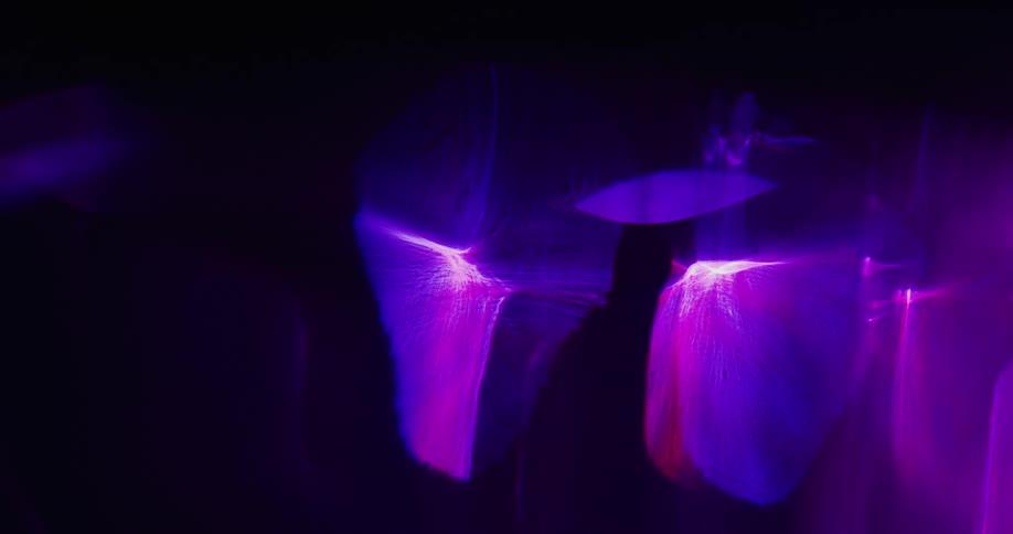 A purple aurora glows in the darkness and shapes flutter as they move away from the aura as if they are in a beam
