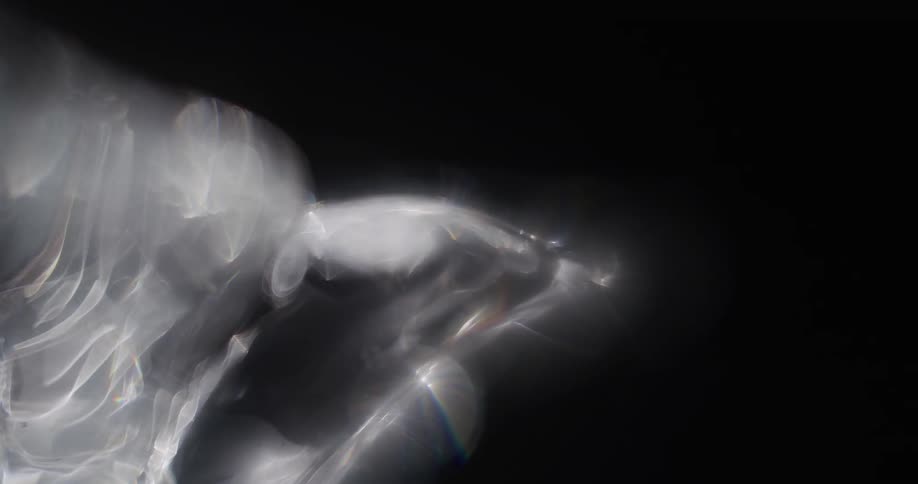 Light shines and reflects off a cloud of smoke swirling and moving across a black background