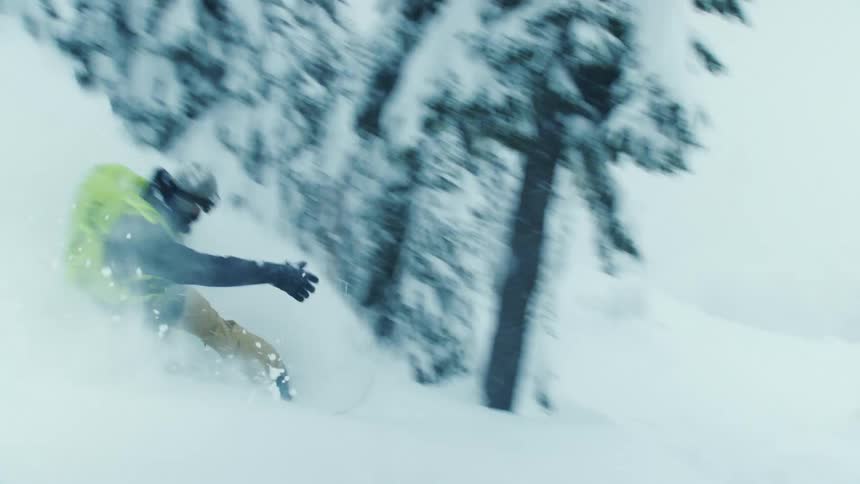 Man riding a snowboard at full speed down the slopes of a mountain covered in white snow