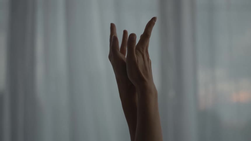 A womans hands and fingers are touching as she raises her arms in the air