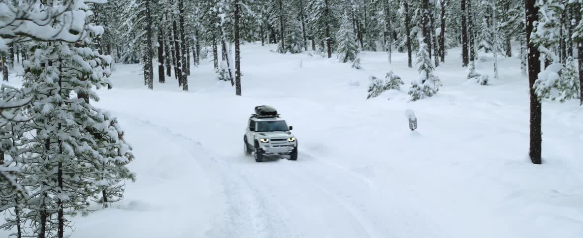 An automobile travels around the bend of a snow covered road through a forest on a winter day