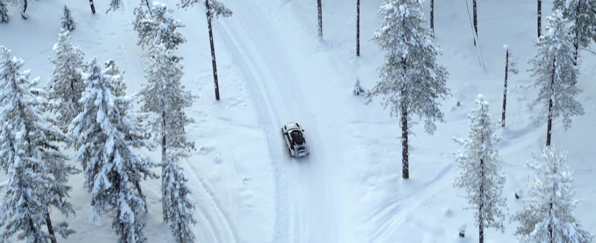An suv with luggage on top slides a bit as it travels on a snow covered road through the trees