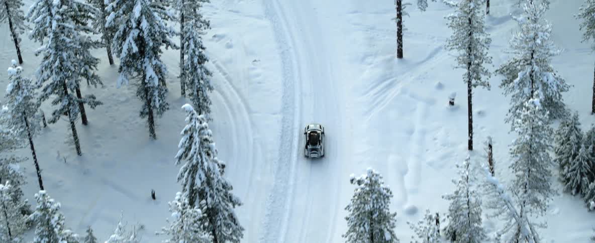 An aerial view of a car driving through a snowy forest on a winter day