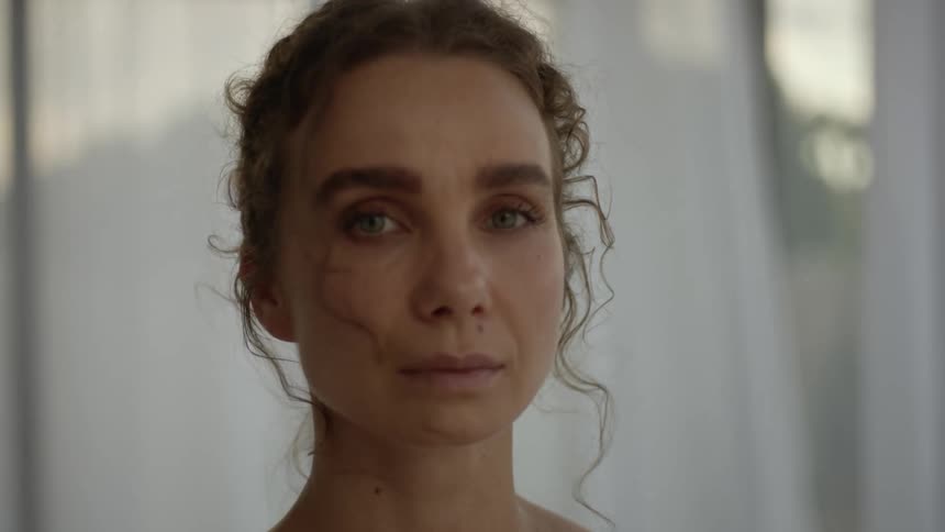 A woman standing in front of a window at home turns her head and looks in front of her