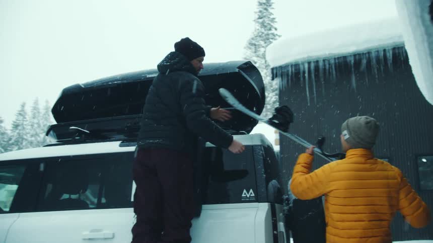 Two male friends are loading their vehicle with snowboarding gear