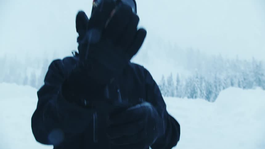 A man standing in the snow pulls on a glove as he gears up