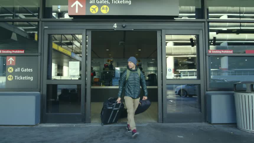Young man carrying luggage exits the airport through an automated door