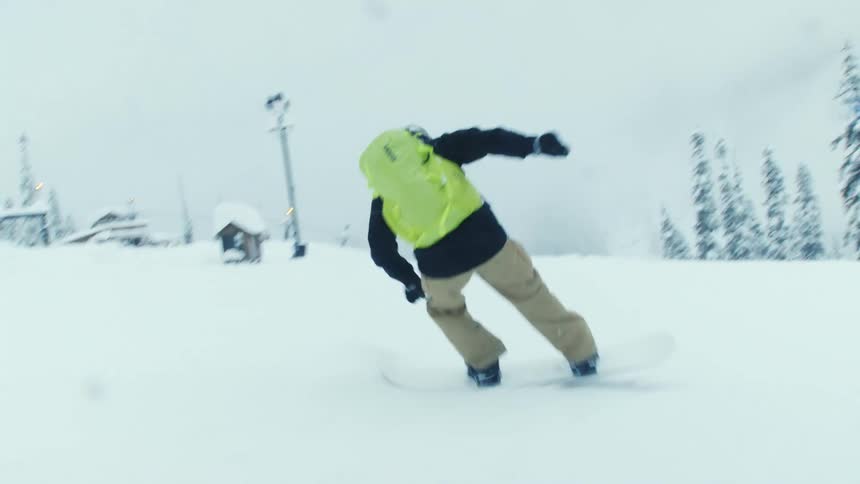 A snowboarder that is traveling downhill at a fast pace spins around to maintain his balance
