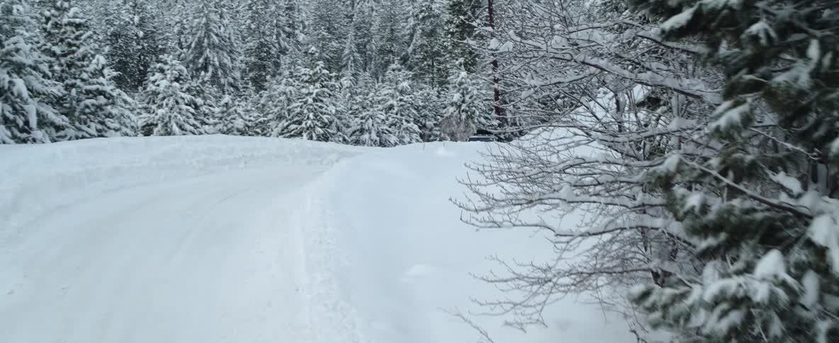 An automobile is traveling on a snow covered road through forested mountains on a winter day