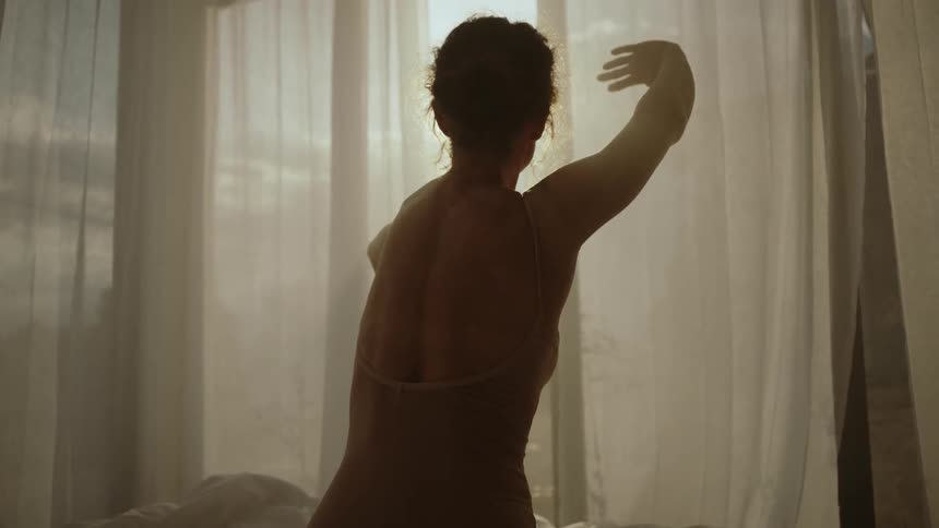 A womanis dancing in a room near a window