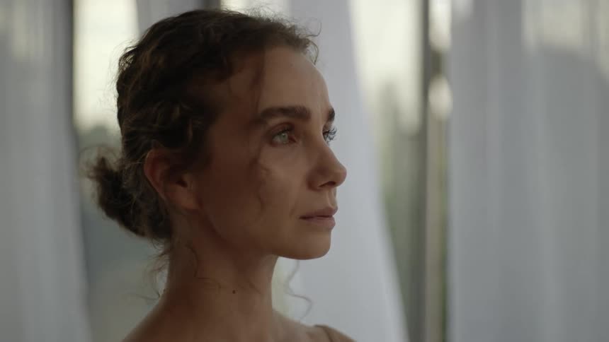 A woman turns her head in dramatic fashion as a breeze blows her hair and curtains