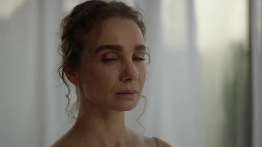 Woman turns her head as curtains waft in breeze behind her