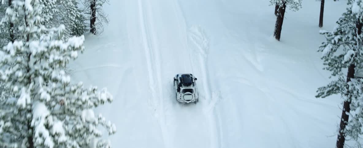 An aerial view of a car driving through a snowy forest in winter