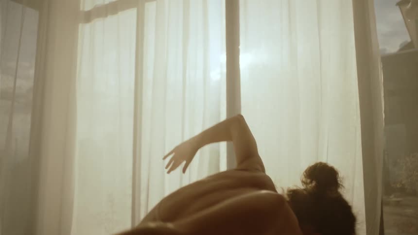 A woman is on a bed with a canopy around it and she is moving her arms doing dance moves