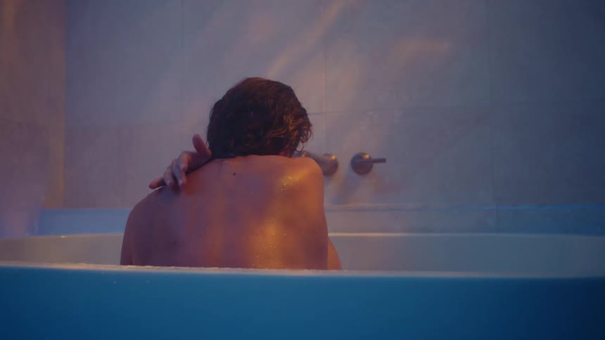 A young white woman is sitting in the bath tub and looking at the wall