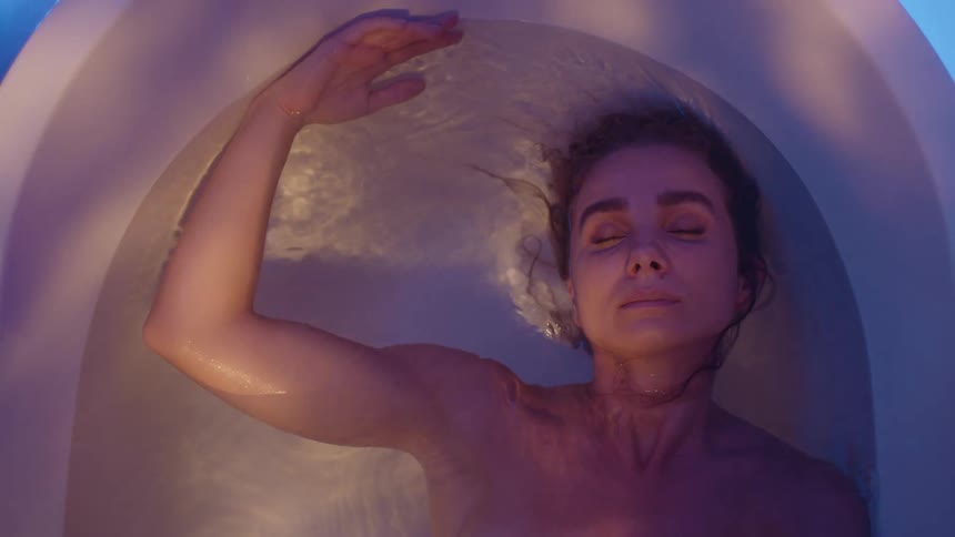 A woman lying in a bathtub full of water moves her head from side to side