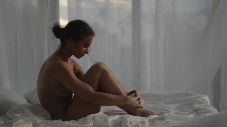 Curtains billow around a woman while she sits in bed